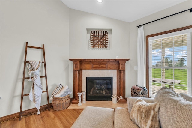 living room featuring a fireplace with flush hearth, vaulted ceiling, light wood-style flooring, and plenty of natural light