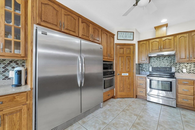 kitchen with glass insert cabinets, decorative backsplash, appliances with stainless steel finishes, and under cabinet range hood