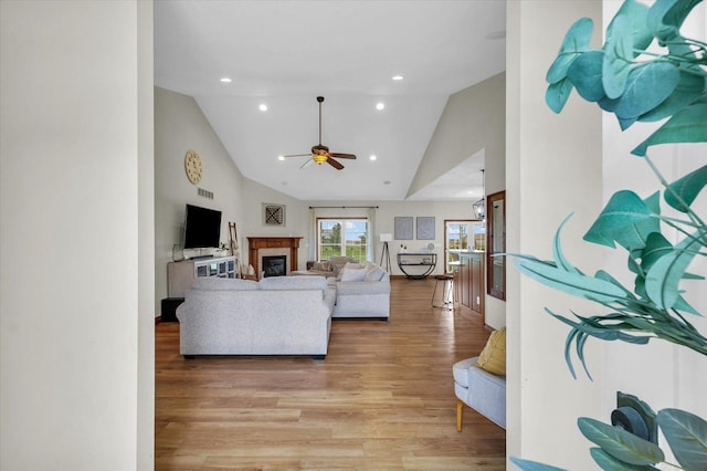 living room featuring light wood-style floors, a glass covered fireplace, high vaulted ceiling, and ceiling fan