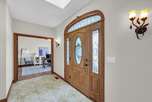foyer featuring baseboards, a skylight, visible vents, and light tile patterned floors