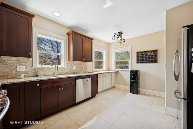 kitchen with a sink, tasteful backsplash, light stone counters, baseboards, and appliances with stainless steel finishes