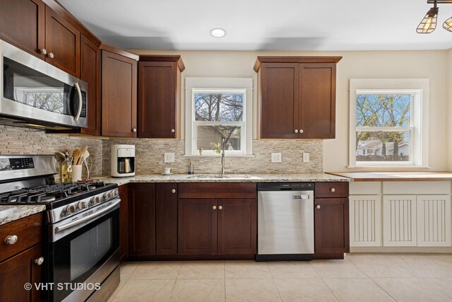 kitchen featuring appliances with stainless steel finishes, light stone counters, backsplash, and a sink
