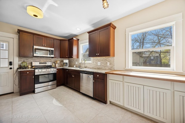 kitchen with light stone countertops, a sink, decorative backsplash, light tile patterned flooring, and appliances with stainless steel finishes