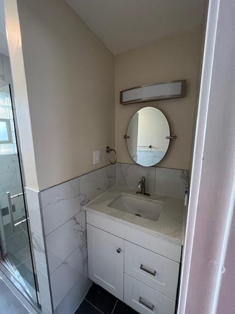 full bath with a stall shower, tile walls, tile patterned floors, vanity, and wainscoting