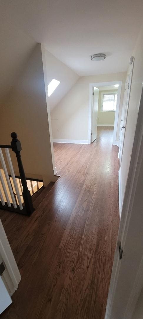 interior space with wood finished floors, an upstairs landing, and vaulted ceiling with skylight