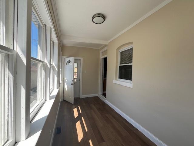 hall with baseboards, visible vents, dark wood-style floors, and crown molding