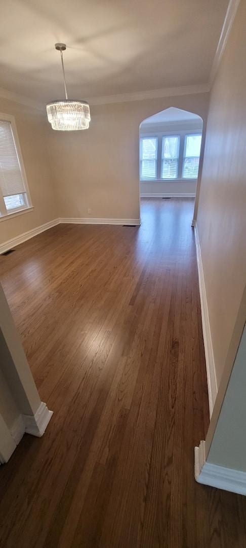 unfurnished dining area with crown molding, visible vents, arched walkways, baseboards, and dark wood-style flooring