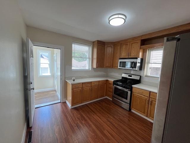 kitchen featuring brown cabinets, stainless steel appliances, light countertops, baseboards, and dark wood finished floors