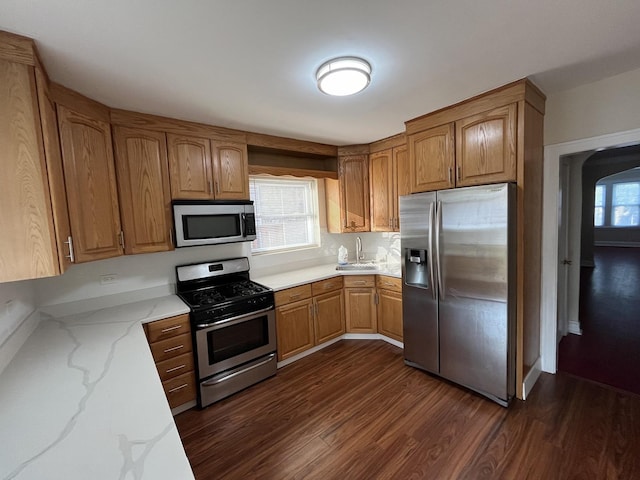 kitchen featuring dark wood-style floors, light stone countertops, a sink, stainless steel appliances, and brown cabinetry