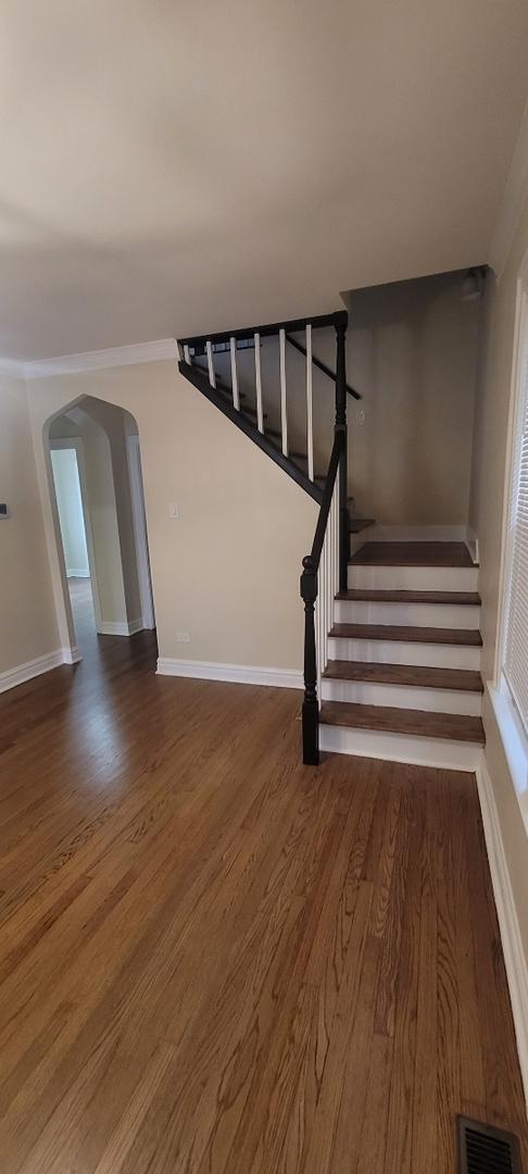 staircase with wood finished floors, baseboards, visible vents, and arched walkways
