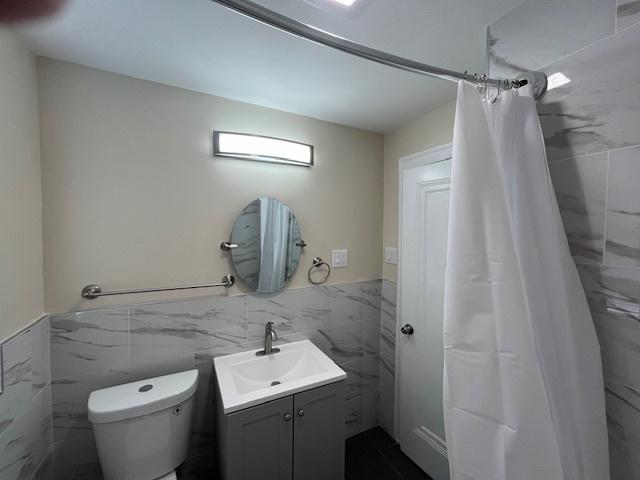 full bath featuring curtained shower, a wainscoted wall, toilet, tile walls, and vanity