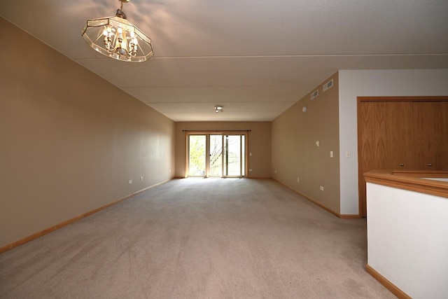 spare room featuring light colored carpet, a chandelier, and baseboards