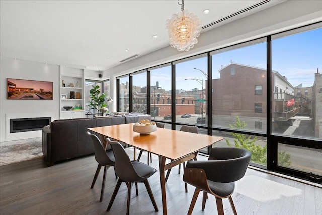 dining space with visible vents, wood finished floors, a fireplace, a chandelier, and built in shelves