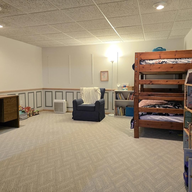 bedroom with a wainscoted wall, a drop ceiling, and carpet floors