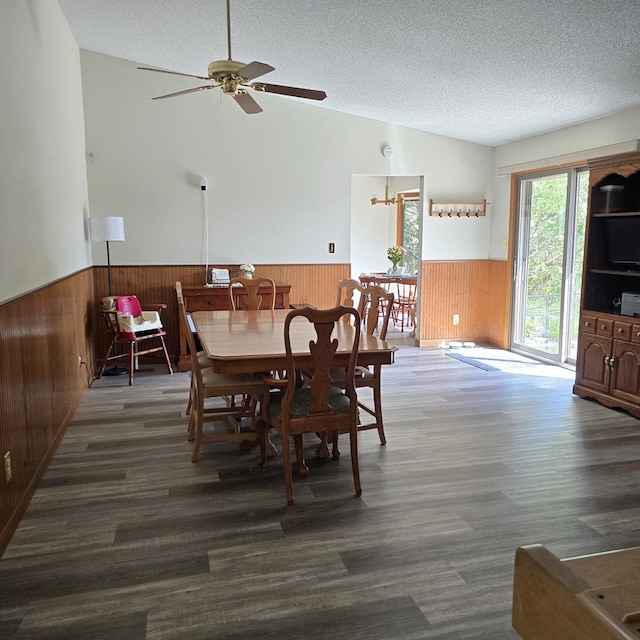 dining area featuring lofted ceiling, a textured ceiling, ceiling fan, a wainscoted wall, and wooden walls