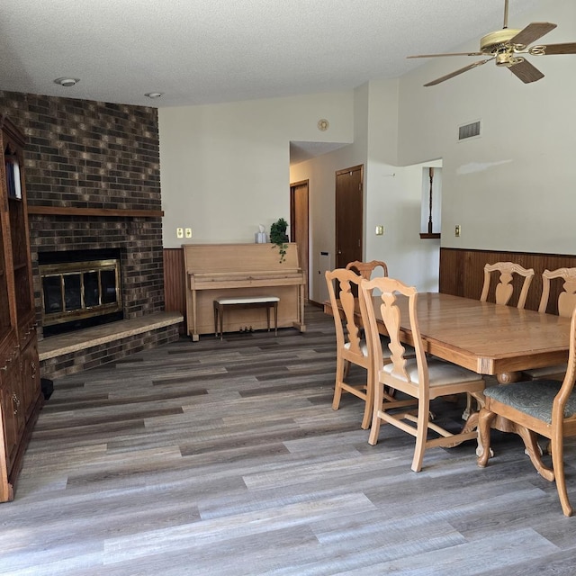 dining space featuring a ceiling fan, visible vents, vaulted ceiling, wainscoting, and wood finished floors