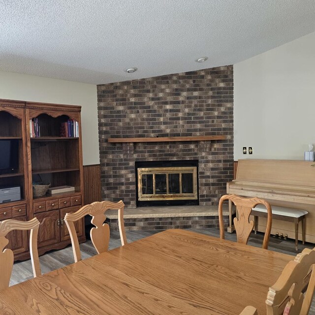 dining area with a textured ceiling, wood finished floors, and a brick fireplace