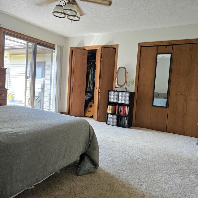 bedroom with carpet, multiple closets, a ceiling fan, and a textured ceiling