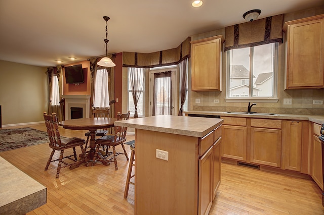 kitchen with a sink, light wood-style floors, a kitchen island, recessed lighting, and a fireplace