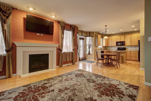 living room with baseboards, light wood-type flooring, a fireplace with flush hearth, and recessed lighting