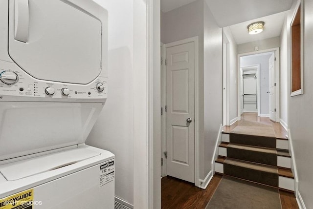 washroom featuring stacked washing maching and dryer, baseboards, and dark wood finished floors