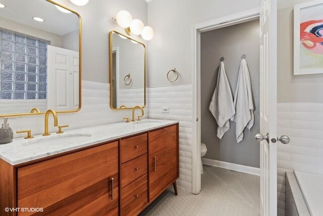 full bath with a sink, tile walls, toilet, and double vanity