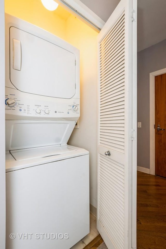 clothes washing area featuring stacked washing machine and dryer, wood finished floors, and baseboards