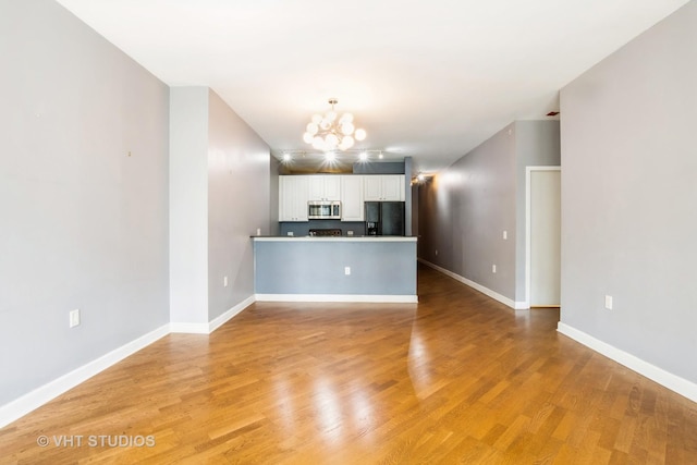 unfurnished living room featuring a chandelier, light wood-style flooring, and baseboards