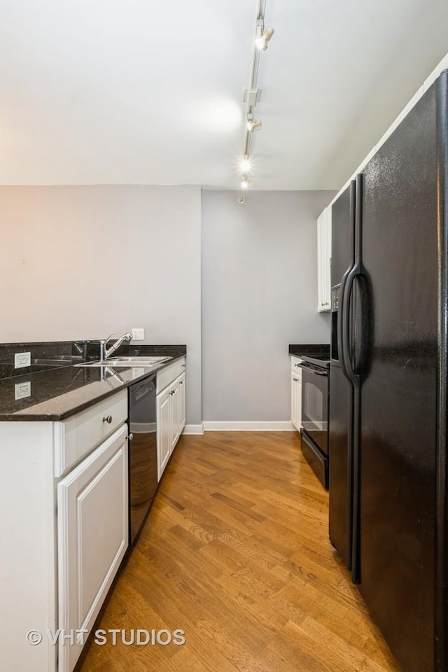 kitchen with black appliances, rail lighting, dark countertops, a sink, and white cabinetry