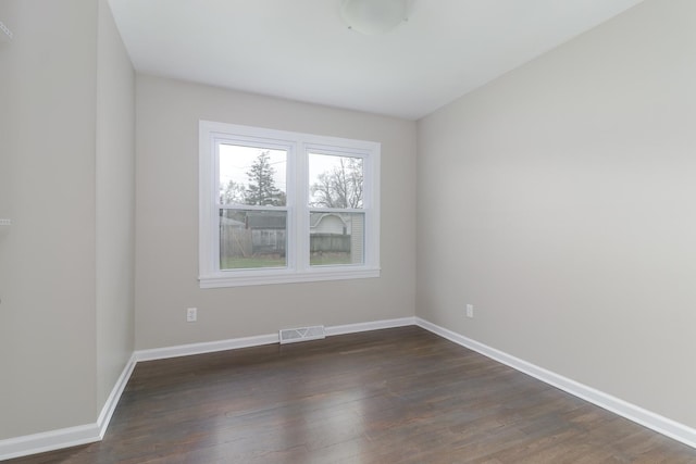 empty room with wood finished floors, visible vents, and baseboards