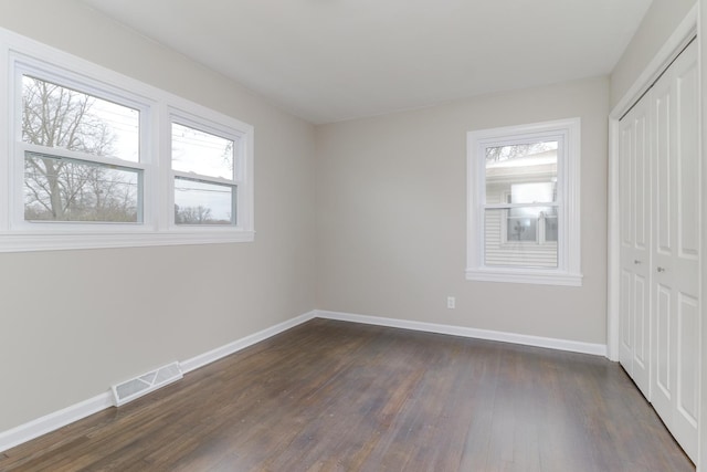 unfurnished bedroom featuring dark wood finished floors, visible vents, a closet, and baseboards