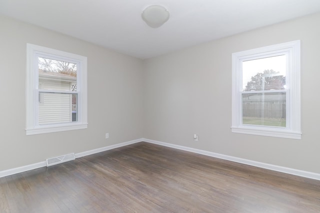 spare room with dark wood finished floors, visible vents, baseboards, and plenty of natural light