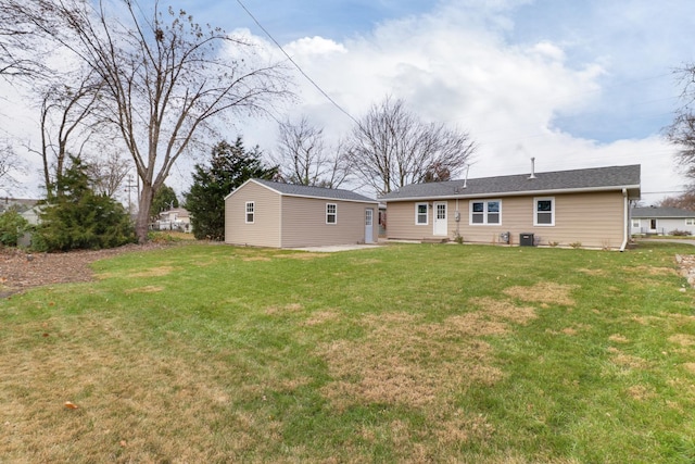 rear view of house featuring a yard, central air condition unit, and an outbuilding