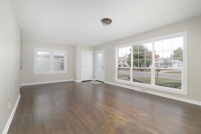 unfurnished living room featuring visible vents, dark wood-style floors, and baseboards
