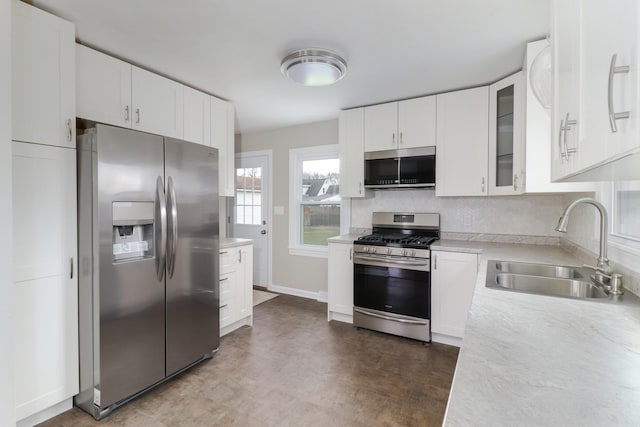 kitchen featuring glass insert cabinets, appliances with stainless steel finishes, light countertops, white cabinets, and a sink