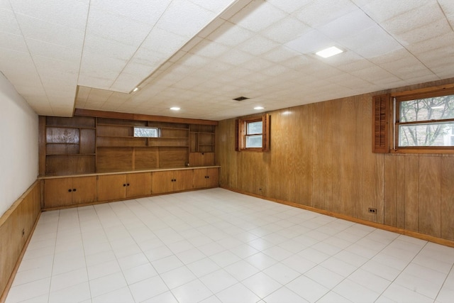 basement featuring wooden walls, visible vents, built in shelves, and light floors