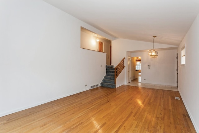 unfurnished living room with visible vents, stairs, baseboards, light wood-style floors, and vaulted ceiling