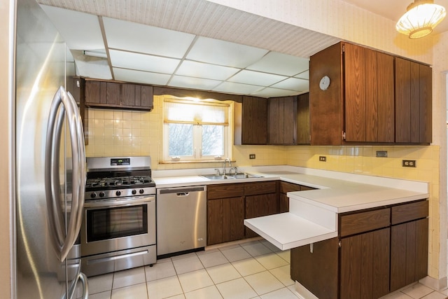 kitchen featuring a peninsula, light tile patterned flooring, light countertops, a sink, and stainless steel appliances