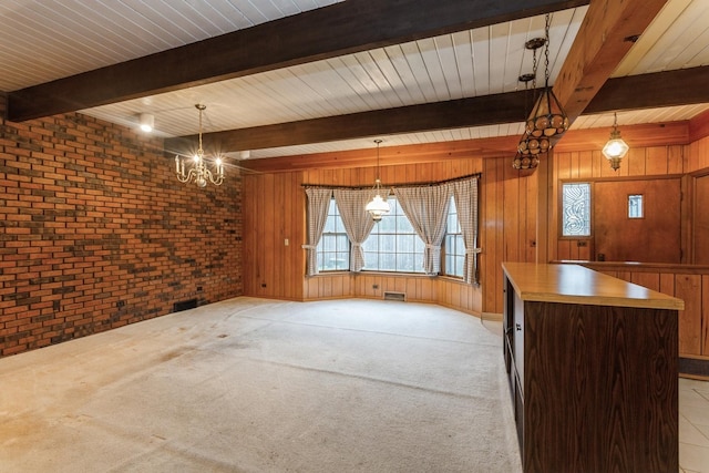 unfurnished dining area with wooden walls, a notable chandelier, beam ceiling, and brick wall