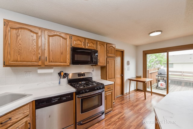 kitchen with a textured ceiling, light wood-style floors, stainless steel appliances, and decorative backsplash