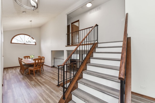 stairs featuring vaulted ceiling, a chandelier, visible vents, and wood finished floors