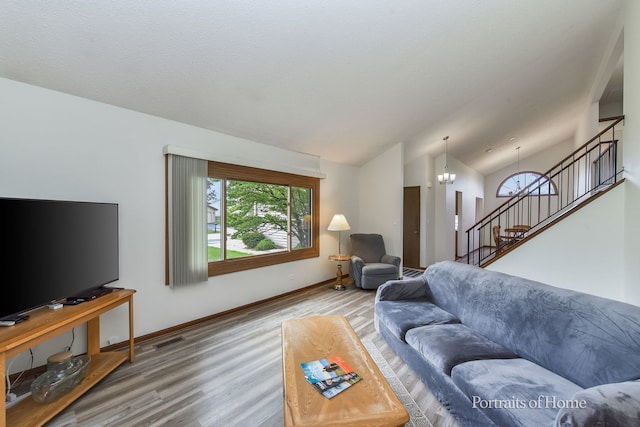 living area with stairs, wood finished floors, vaulted ceiling, an inviting chandelier, and baseboards