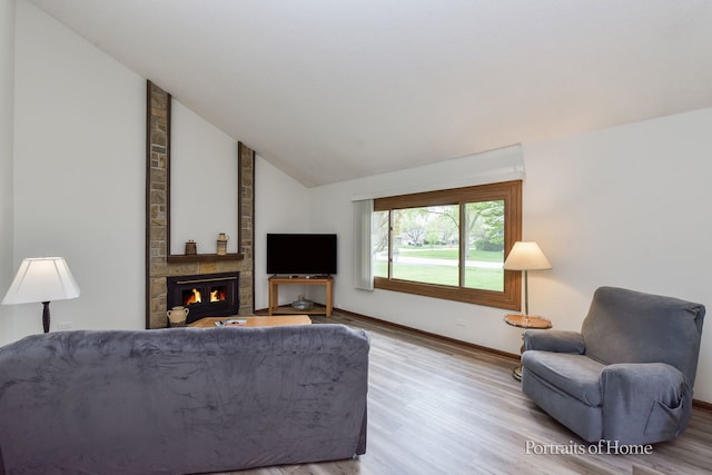 living area featuring baseboards, vaulted ceiling, a large fireplace, and wood finished floors