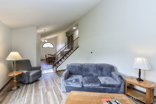 living area featuring an inviting chandelier, stairs, baseboards, and wood finished floors
