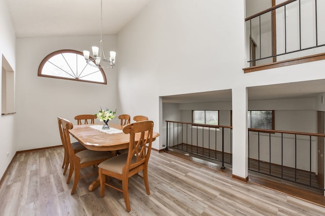 dining space featuring an inviting chandelier, wood finished floors, a towering ceiling, and a healthy amount of sunlight