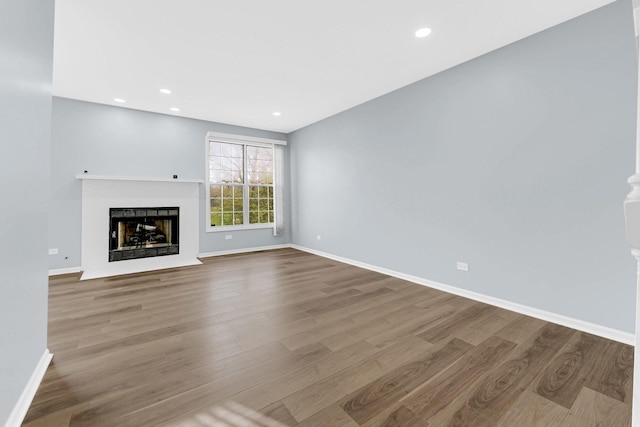 unfurnished living room featuring a fireplace with flush hearth, baseboards, recessed lighting, and wood finished floors