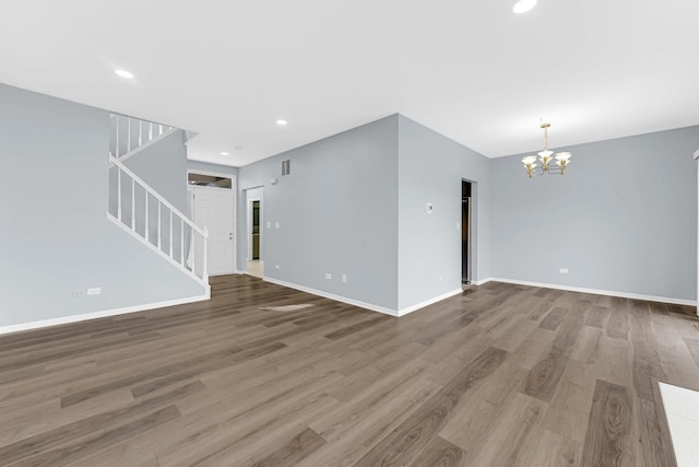 unfurnished living room with stairs, baseboards, an inviting chandelier, and wood finished floors