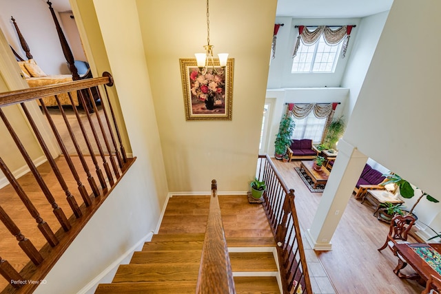 stairway with a high ceiling, a notable chandelier, wood finished floors, and baseboards