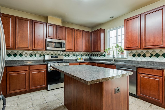 kitchen with a sink, decorative backsplash, light tile patterned floors, dark countertops, and appliances with stainless steel finishes