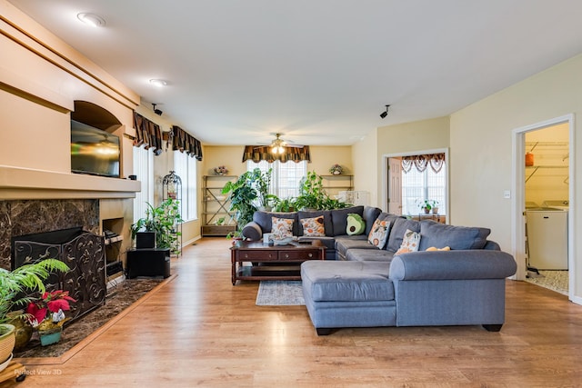living area featuring a high end fireplace, a ceiling fan, light wood-style flooring, and washer / clothes dryer